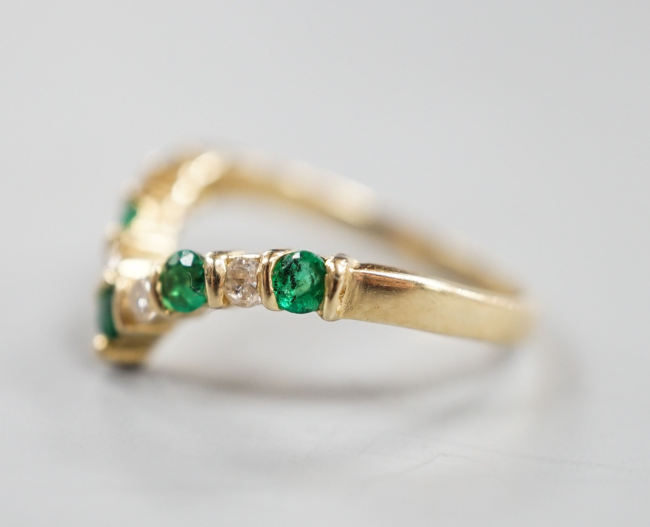 A modern 14k yellow metal, five stone emerald and four stone diamond set wishbone ring, size M, gross 2.3 grams.